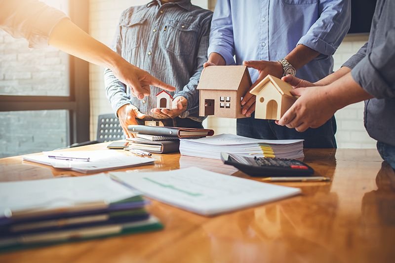 People holding model houses above property documents
