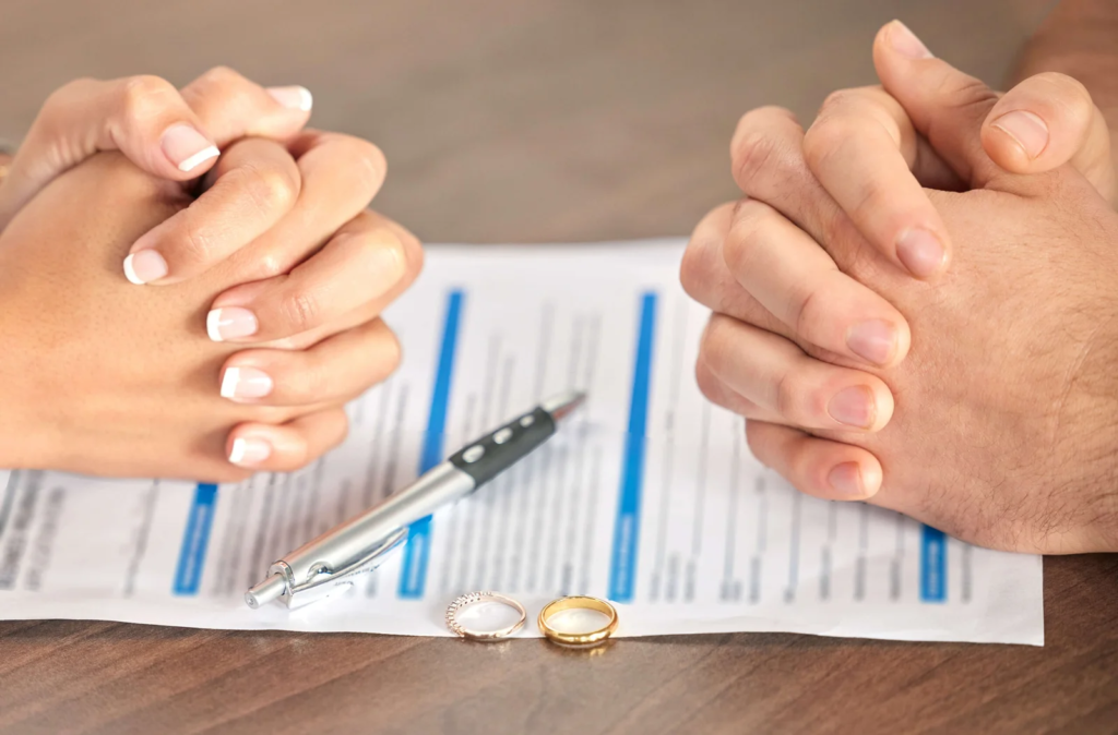 Clasped hands beside an agreement, pen and wedding rings