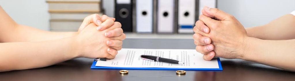 Two people seated across an agreement with wedding rings on the table
