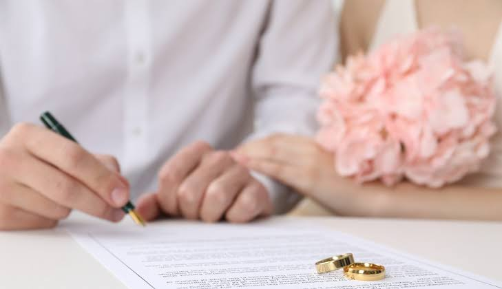 Couple signing a document beside wedding rings